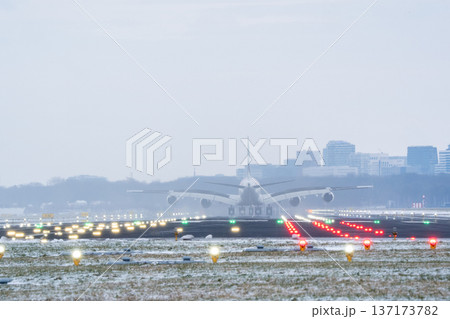 Commercial aircraft approaching the runway during a snowy evening with city skyline 137173782