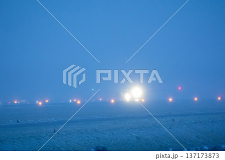Bright landing lights of a passenger aircraft approaching the runway through dense morning fog at the international airport Bright landing lights of a passenger aircraft approaching the runway through dense morning fog at the international airport 137173873