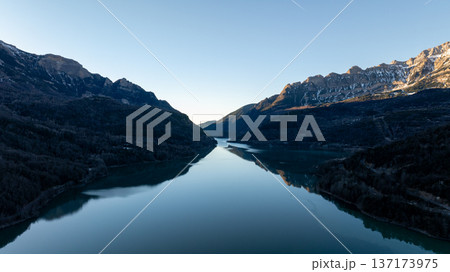 Symmetric view of a long mountain reservoir stretching through a steep valley under a clear blue sky 137173975
