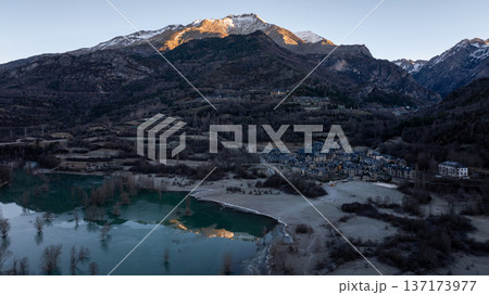 Picturesque view of a traditional stone village located next to a bright blue mountain lake under snowy peaks Picturesque view of a traditional stone village located next to a bright blue mountain lake under snowy peaks 137173977