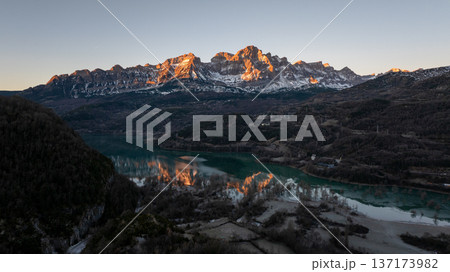 Beautiful winter landscape featuring snow capped mountains illuminated by the setting sun with a clear reflection in the water Beautiful winter landscape featuring snow capped mountains illuminated by the setting sun with a clear reflection in the water 137173982
