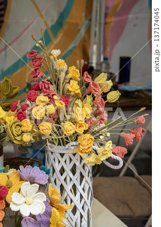Crochet flowers arranged in vase on table with handmade knitted bouquet in yellow and pink colors inside wicker basket. Concept of craft crochet flowers decor, craft hobby, handmade gift idea 137174045