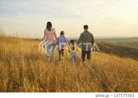 Parents and children walking in golden meadow at sunset, family togetherness Parents and children walking in golden meadow at sunset, family togetherness 137175501