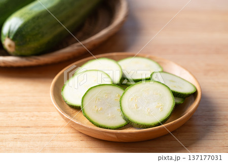 Slices of fresh green zucchini in a wooden plate, ready for healthy cooking 137177031