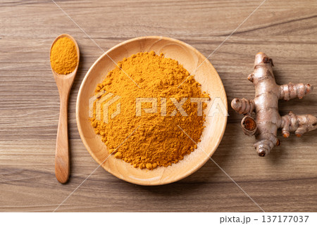 Turmeric powder in a wooden bowl with a wooden spoon and fresh turmeric roots on a wooden background 137177037