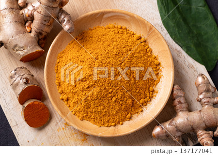 Turmeric powder in a wooden bowl and fresh turmeric roots 137177041