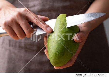 Close up of hand holding knife and peeling green mango 137177042