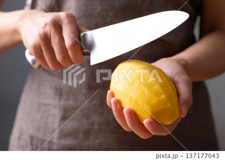 Close up of hand holding peeled mango and slicing with a knife Close up of hand holding peeled mango and slicing with a knife 137177043