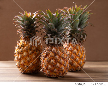 Three whole fresh ripe pineapples on a brown wooden background, Tropical fruit in summer season Three whole fresh ripe pineapples on a brown wooden background, Tropical fruit in summer season 137177049