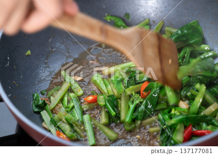 Hand using a wooden spatula to stir-fry Chinese kale with soy sauce in a pan 137177081