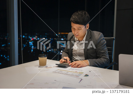 businessman analyzing financial reports and using calculator to data analysis in business office with city lights background at night businessman analyzing financial reports and using calculator to data analysis in business office with city lights background at night 137179181