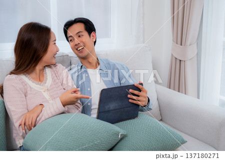 Happy asian couple video call on tablet together in living room at home. Happy asian couple video call on tablet together in living room at home. 137180271