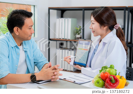 Asian woman nutritionist showing AI BMI calculator on tablet and explaining to man patient. Asian woman nutritionist showing AI BMI calculator on tablet and explaining to man patient. 137180272