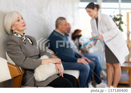 Elderly woman sitting in clinic queue while nurse talks to other patients Elderly woman sitting in clinic queue while nurse talks to other patients 137180400