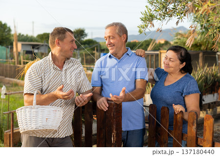 Smiling elderly couple talking to male neighbor near wooden fence in garden 137180440