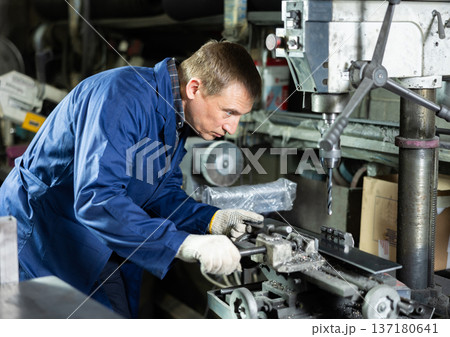 Wworkman drilling metal parts on stationary machine in metalworking workshop 137180641