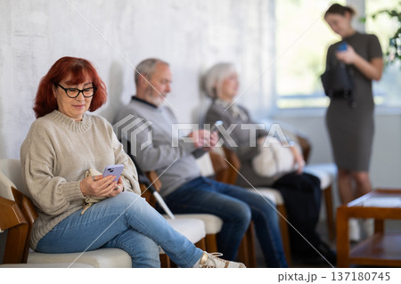 Elderly woman sitting in clinic waiting area scrolling mobile phone Elderly woman sitting in clinic waiting area scrolling mobile phone 137180745