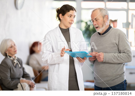 Young nurse or doctor talking with elderly man in reception area Young nurse or doctor talking with elderly man in reception area 137180814