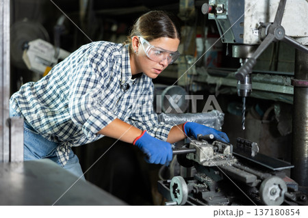 Girl worker at metallurgical plant drills hole in metal plate using drilling machine 137180854