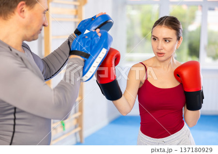 Young girl training boxing kicks on punch mitts held by male instructor 137180929