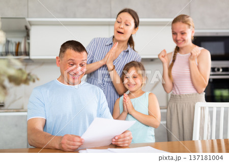 Happy man with wife and teenage daughters reading notification at home Happy man with wife and teenage daughters reading notification at home 137181004