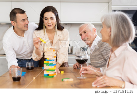 Joyful senior parents and young couple sitting around table playing brick game 137181119