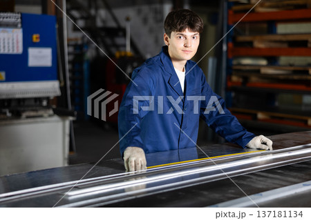Guy working at metallurgical plant carefully measures sheet of iron using tape measure Guy working at metallurgical plant carefully measures sheet of iron using tape measure 137181134