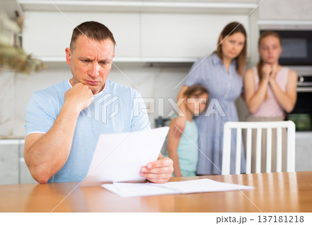 Worried wife and daughters are watching looking at upset and reading documents of father of family 137181218