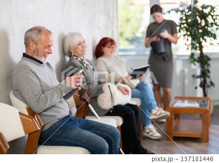 Elderly man and woman in casual clothes waiting for turn on chair in reception Elderly man and woman in casual clothes waiting for turn on chair in reception 137181446