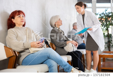 Elderly woman sitting in clinic queue while nurse talks to other patients Elderly woman sitting in clinic queue while nurse talks to other patients 137181504