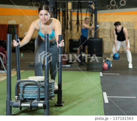 Concentrated young girl performing intense sled pushing in gym 137181563