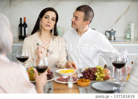 Mature married couple are sitting at table, enjoying food and wine with middle-aged guests. 137181619