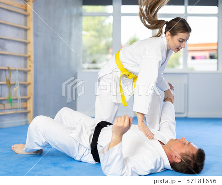 Woman and man practice grabbing and throwing on sports mats during judo training in gym Woman and man practice grabbing and throwing on sports mats during judo training in gym 137181656