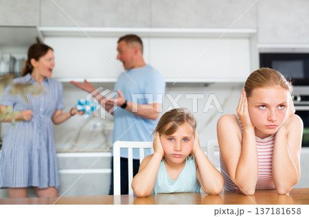 Frightened and frowning children sit at kitchen table during mom and dad quarrel. 137181658