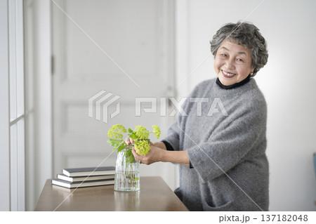 部屋に花を飾るシニア女性 カメラ目線で笑顔のポートレート 部屋に花を飾るシニア女性 カメラ目線で笑顔のポートレート 137182048