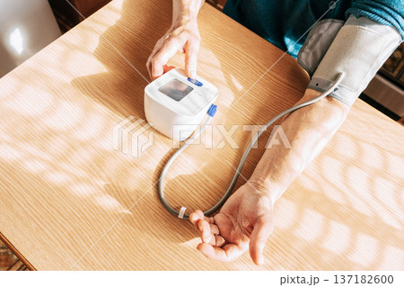 An elderly woman measures her blood pressure in the kitchen. Health maintenance, healthy aging, disease prevention, cardiovascular system monitoring, home treatment An elderly woman measures her blood pressure in the kitchen. Health maintenance, healthy aging, disease prevention, cardiovascular system monitoring, home treatment 137182600