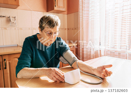 An elderly woman measures her blood pressure in the kitchen. Health maintenance, healthy aging, disease prevention, cardiovascular system monitoring, home treatment 137182603