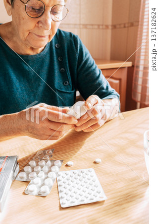 An elderly woman carefully reads the instructions on a bottle of medication. Age-related medication confusion, problems with home care, and medication hesitancy 137182624