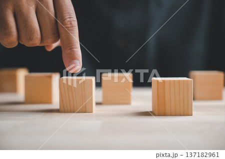 A hand points at a wooden block in a row of blocks. Concept for choice, decision, or opportunity. A hand points at a wooden block in a row of blocks. Concept for choice, decision, or opportunity. 137182961