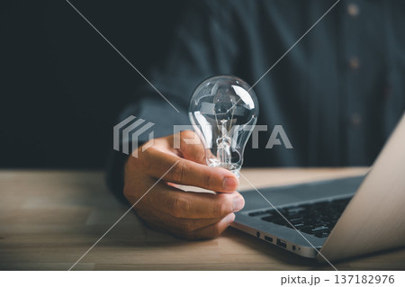 Hand holding a light bulb over a laptop keyboard, representing new ideas and innovation. Hand holding a light bulb over a laptop keyboard, representing new ideas and innovation. 137182976