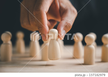 A hand carefully lifting a wooden figure from a group of figures. A hand carefully lifting a wooden figure from a group of figures. 137182979