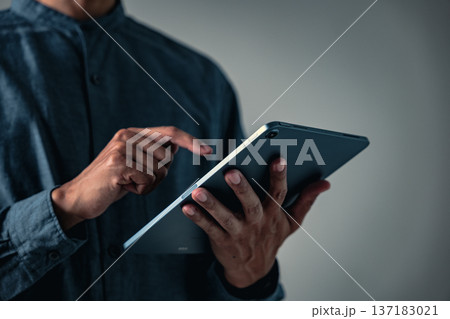 A professional man in a focused pose uses a hand gesture while holding a digital tablet, a great business pose for concepts about technology and modern communication 137183021