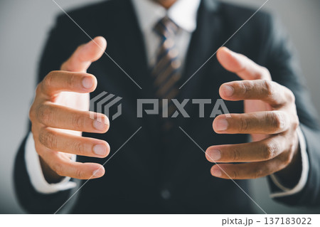 Close-up of a man's hands, with a blurred suit jacket and tie in the background, holding something unseen. 137183022