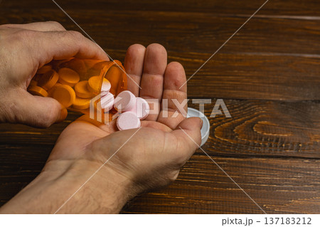 Hands holding a pill bottle and pouring tablets into a palm 137183212