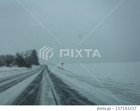 Snowy road during winter with trees and snow-covered field in the distance Snowy road during winter with trees and snow-covered field in the distance 137183217