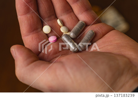 Hand holding different types of pills and capsules on a wooden surface Hand holding different types of pills and capsules on a wooden surface 137183239