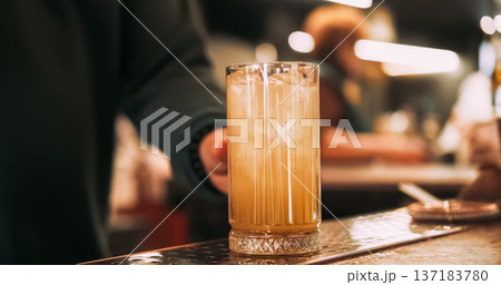 Prepared beverage. Bartender work. Man hand putting cocktail shiny glass on pub counter. Tasty refreshing yellow drink with ice cubes. 137183780