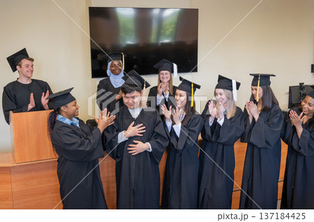 Young multinational people in graduation gowns congratulate each other on graduation from university. Young multinational people in graduation gowns congratulate each other on graduation from university. 137184425