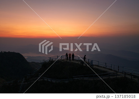 Silhouette of tourists standing on a mountain ridge viewpoint watching a spectacular sunrise and sea of fog. 137185018