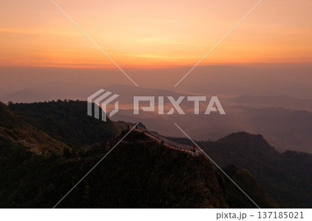 Aerial view of a mountain ridge path with a fence overlooking a breathtaking valley and sea of clouds at sunrise. Aerial view of a mountain ridge path with a fence overlooking a breathtaking valley and sea of clouds at sunrise. 137185021